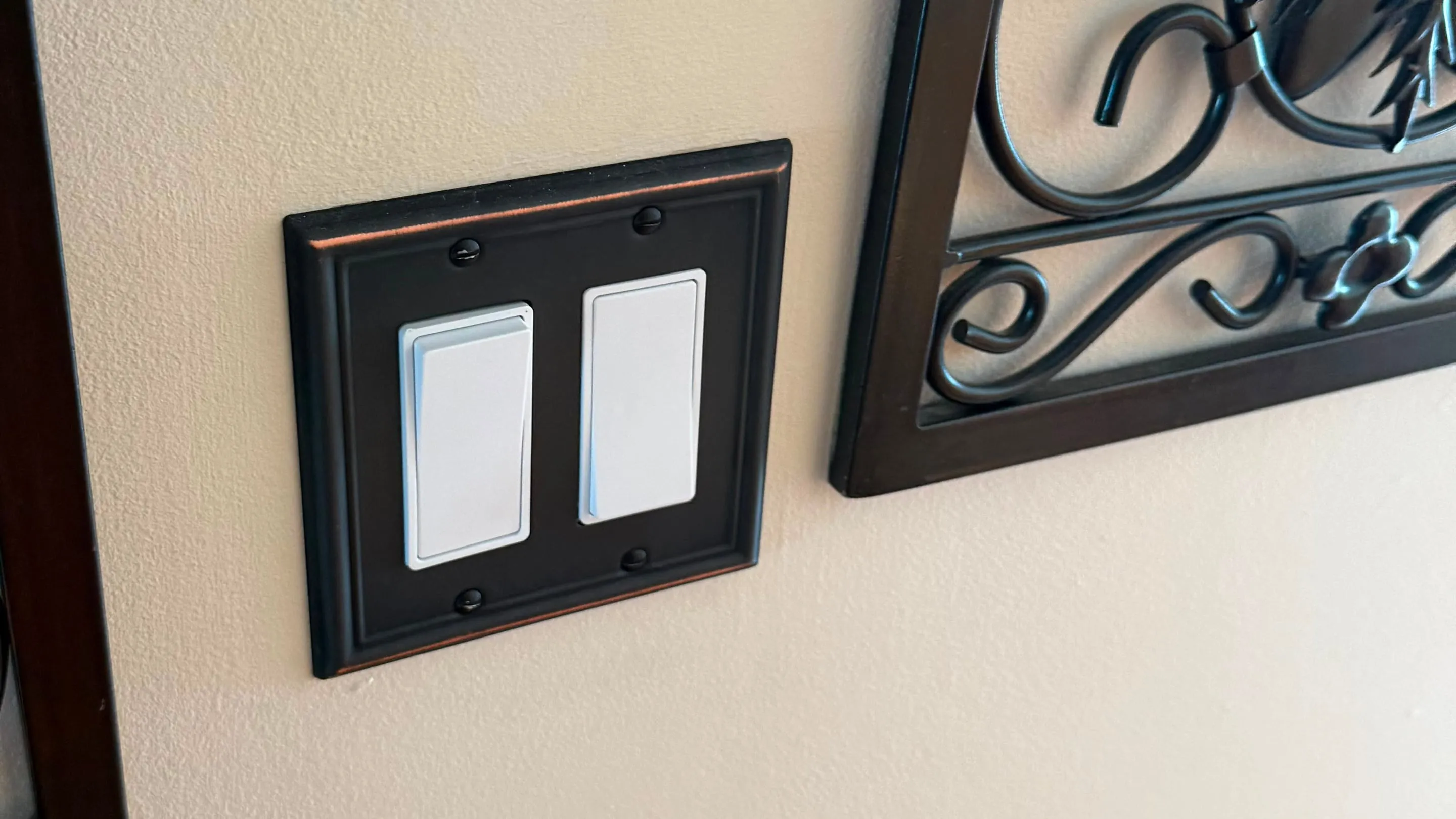 Two white decora rocker switches in an oil-rubbed bronze wall plate installed on a cream wall