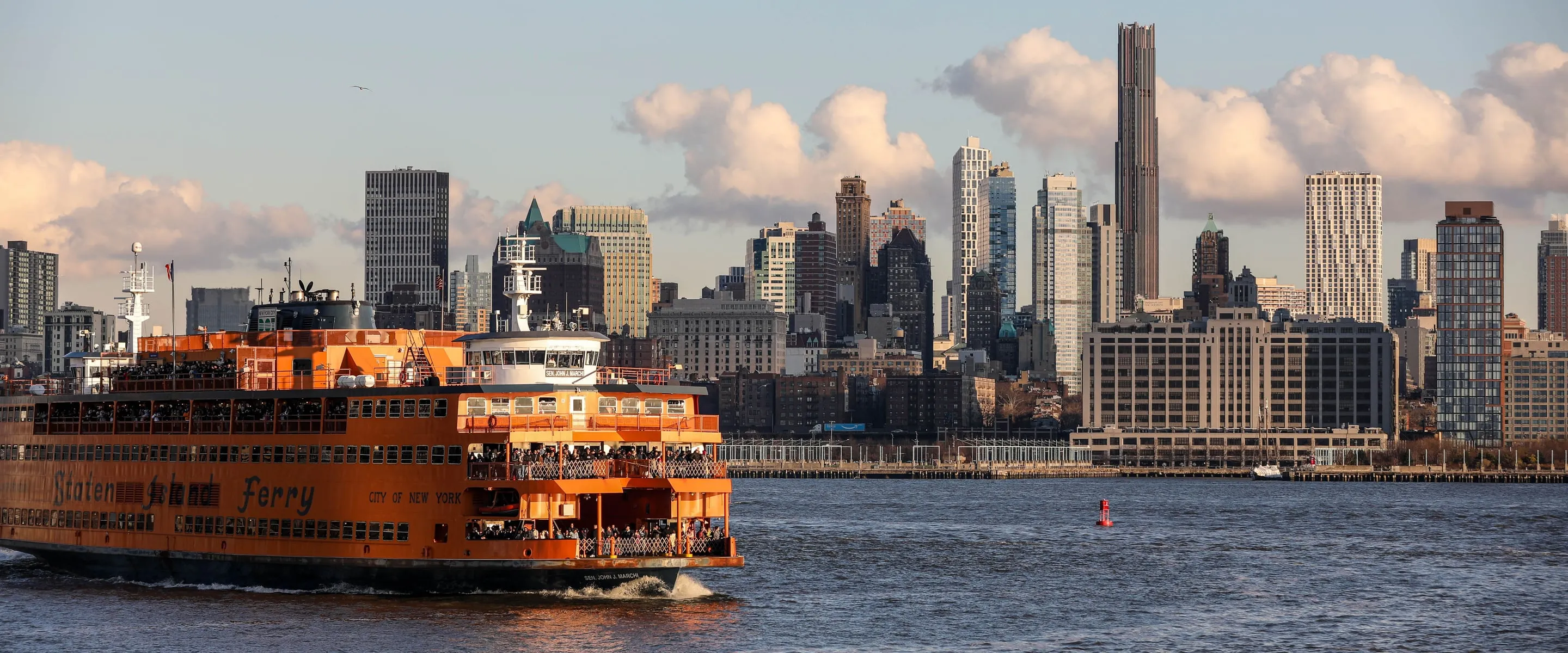 The Staten Island Ferry crossing New York Harbor at golden hour with the Brooklyn skyline behind it